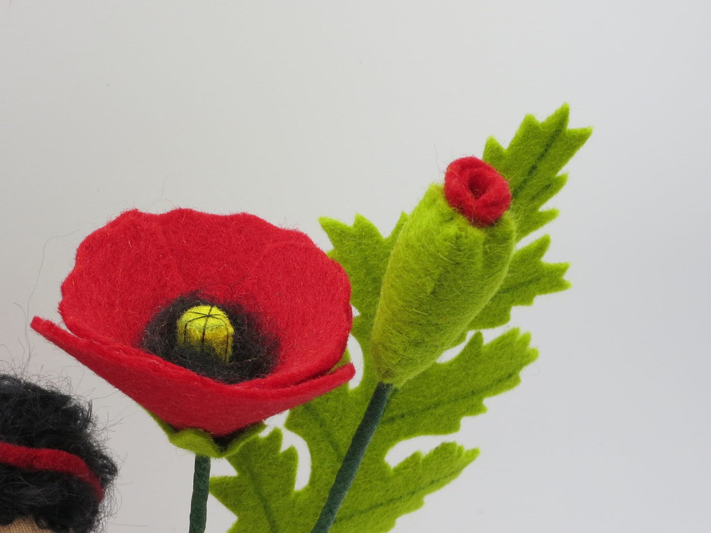 Nahaufnahme der Mohnblüten-Mitte aus Wollfilz mit schwarzem Fransenkranz und gelber Samenkapsel.