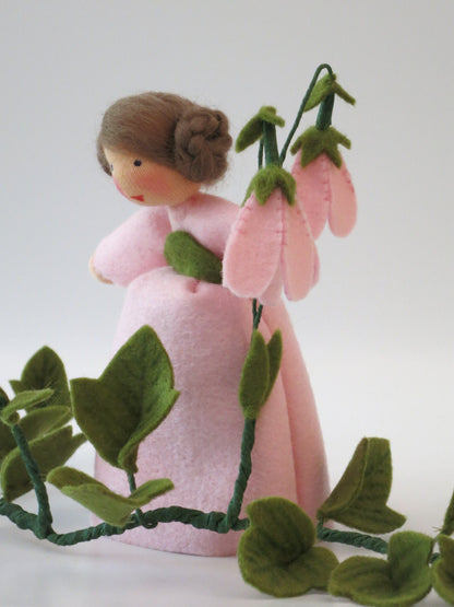 Rückansicht des Moosglöckchen-Blumenkindes mit vier Glöckchenblüten und Zopfschnecken.