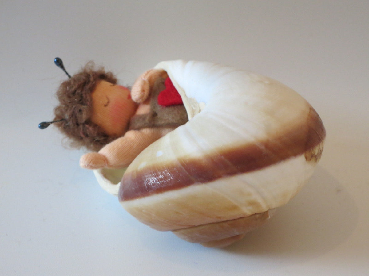 Müdes Schneckchen im echten Schneckenhaus mit brauner Streifenzeichnung, Wollfilzfigur für den Jahreszeitentisch.
