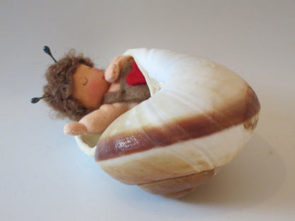 Müdes Schneckchen im echten Schneckenhaus mit brauner Streifenzeichnung, Wollfilzfigur für den Jahreszeitentisch.