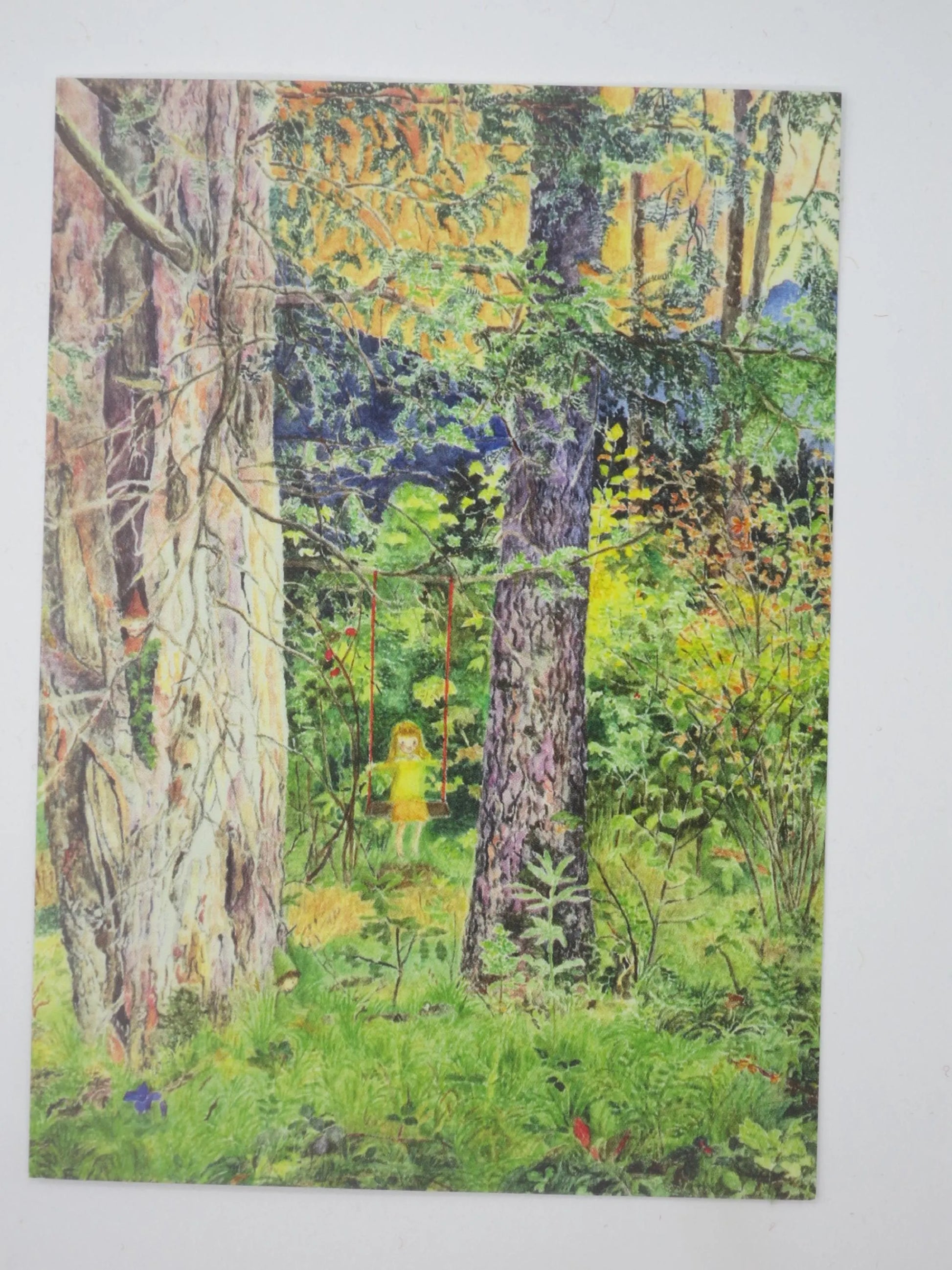 Postkarte Zwischen Eibe und Tanne von Elisabeth Heuberger: Mädchen schaukelt zwischen zwei Nadelbäumen