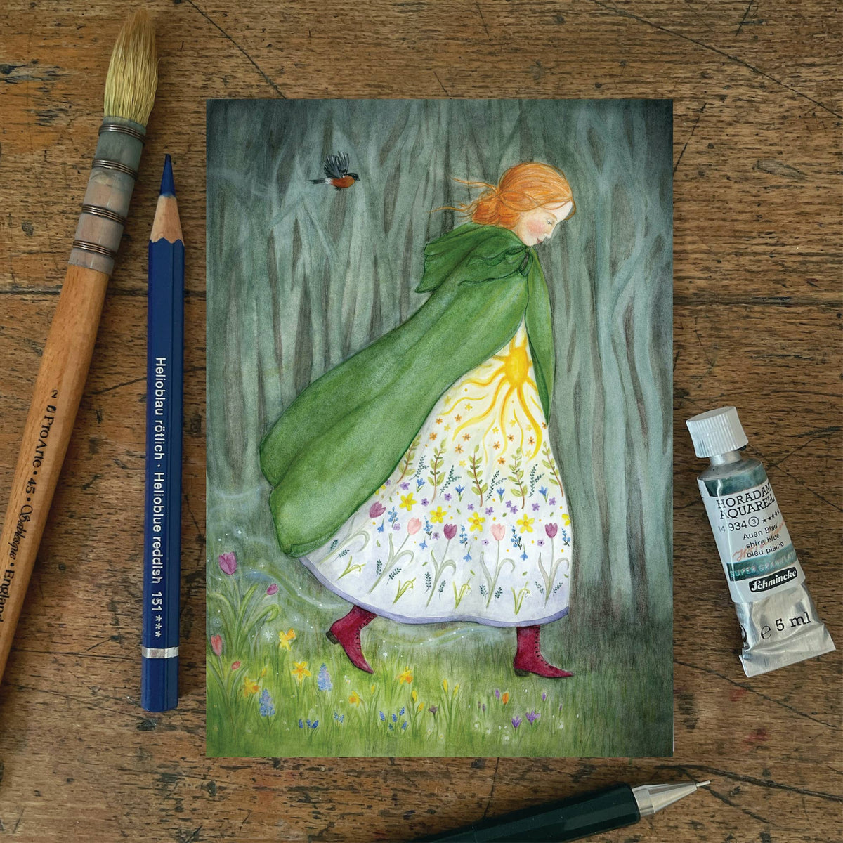 Waldorf Postkarte Ankunft des Frühlings PKFR230: Gestalt im grünen Umhang und Blütenkleid schreitet aus dem grauen Wald auf eine blühende Wiese, ein Rotkehlchen fliegt voraus. Aquarell von Mhairi Hellbrandt