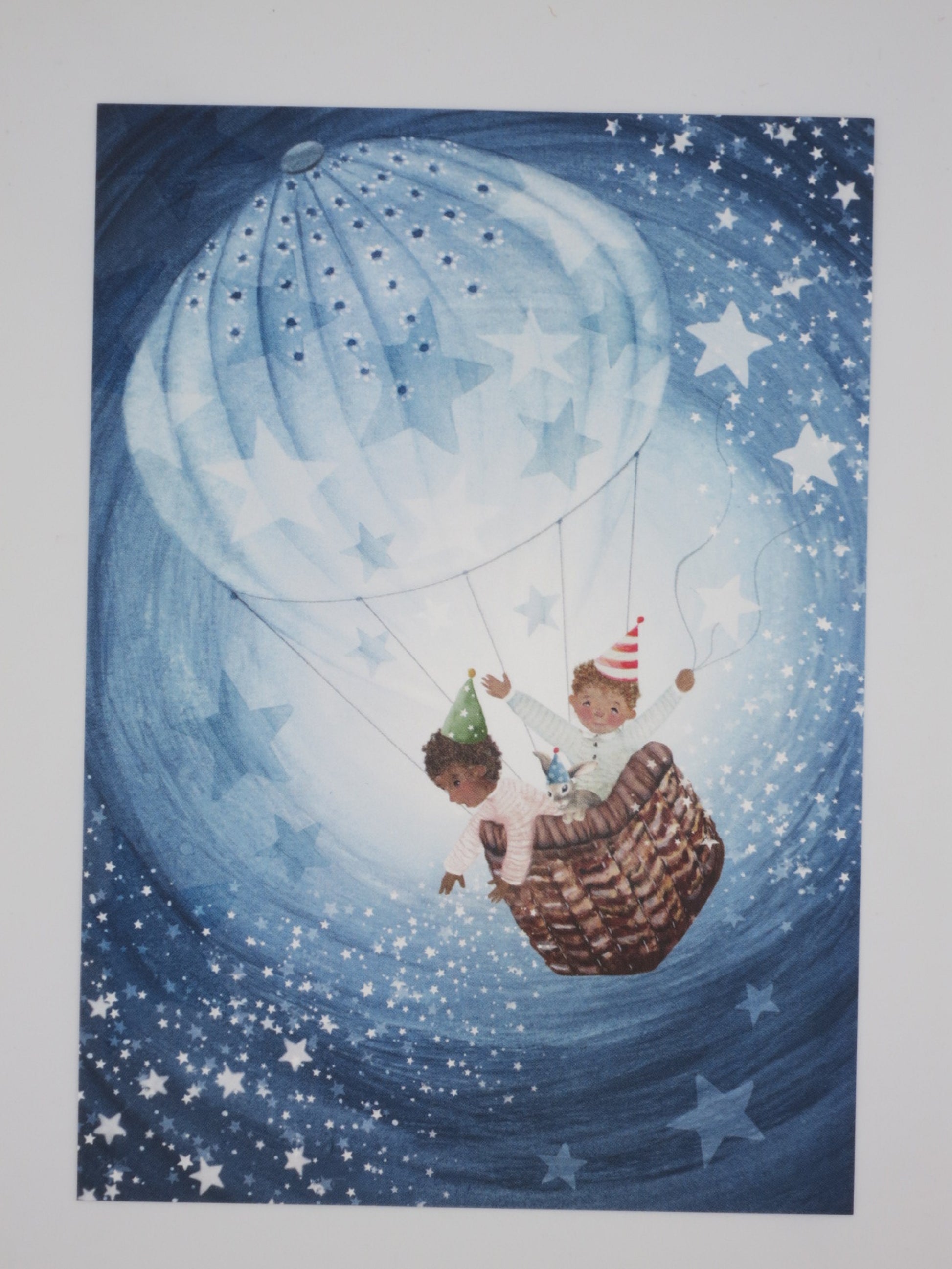 Postkarte Bis zum Mond und zurück: Kinder mit Partyhüten im Ballonkorb unter Sternenhimmel, Illustration von Bijdehansje