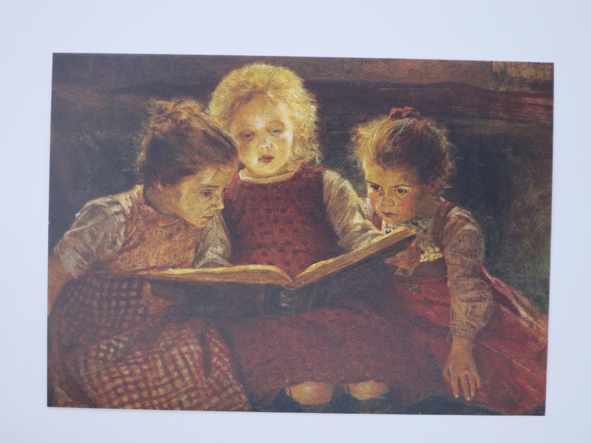 Drei Kinder lesen gemeinsam vertieft in einem Buch im warmen Licht – Postkarte Ein gutes Buch von Walther Firle