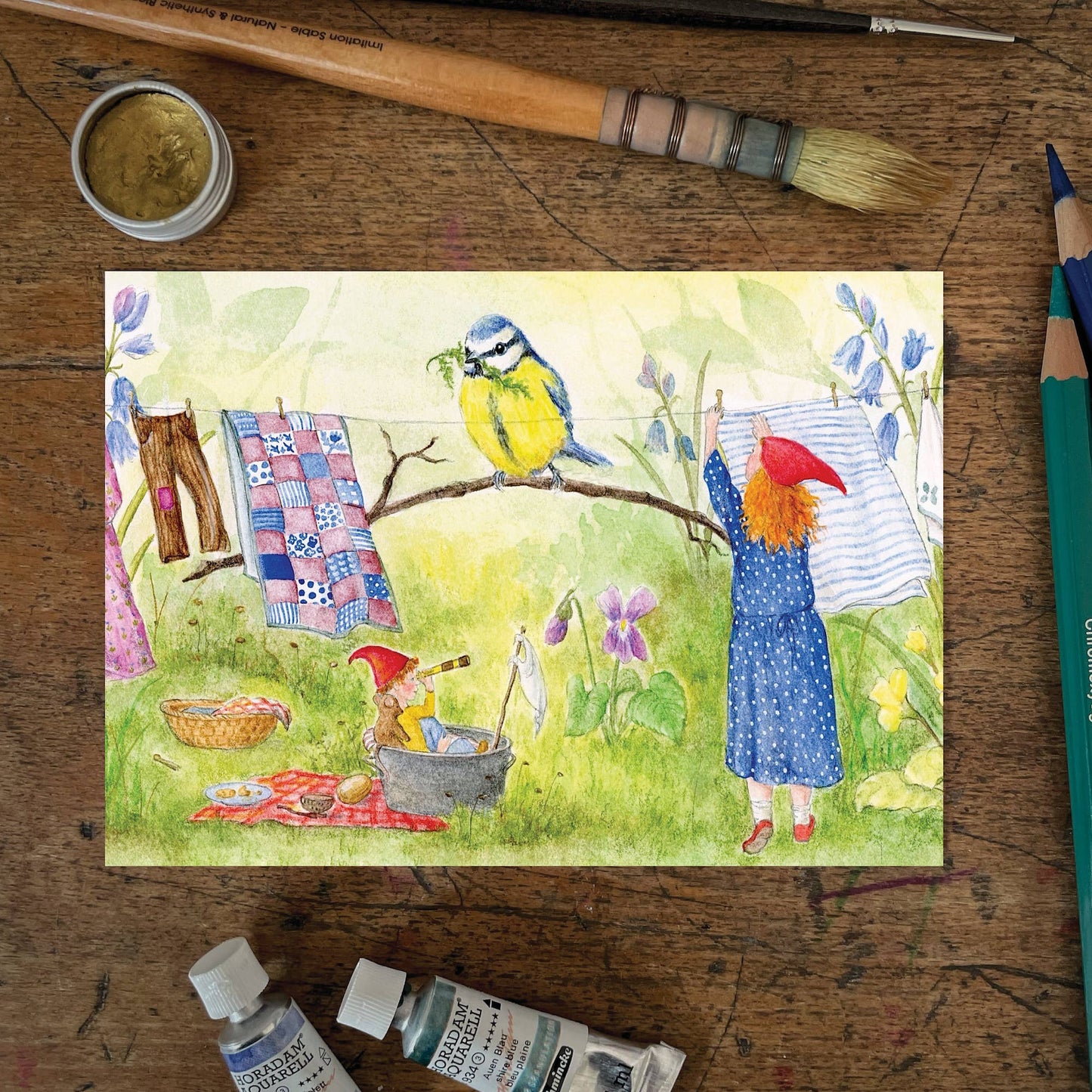 Frühlings Postkarte Frühlingswäsche PKFR231: Wichtelmädchen hängt Wäsche im Garten auf 
Zeichnung von Mhairi Hellbrandt