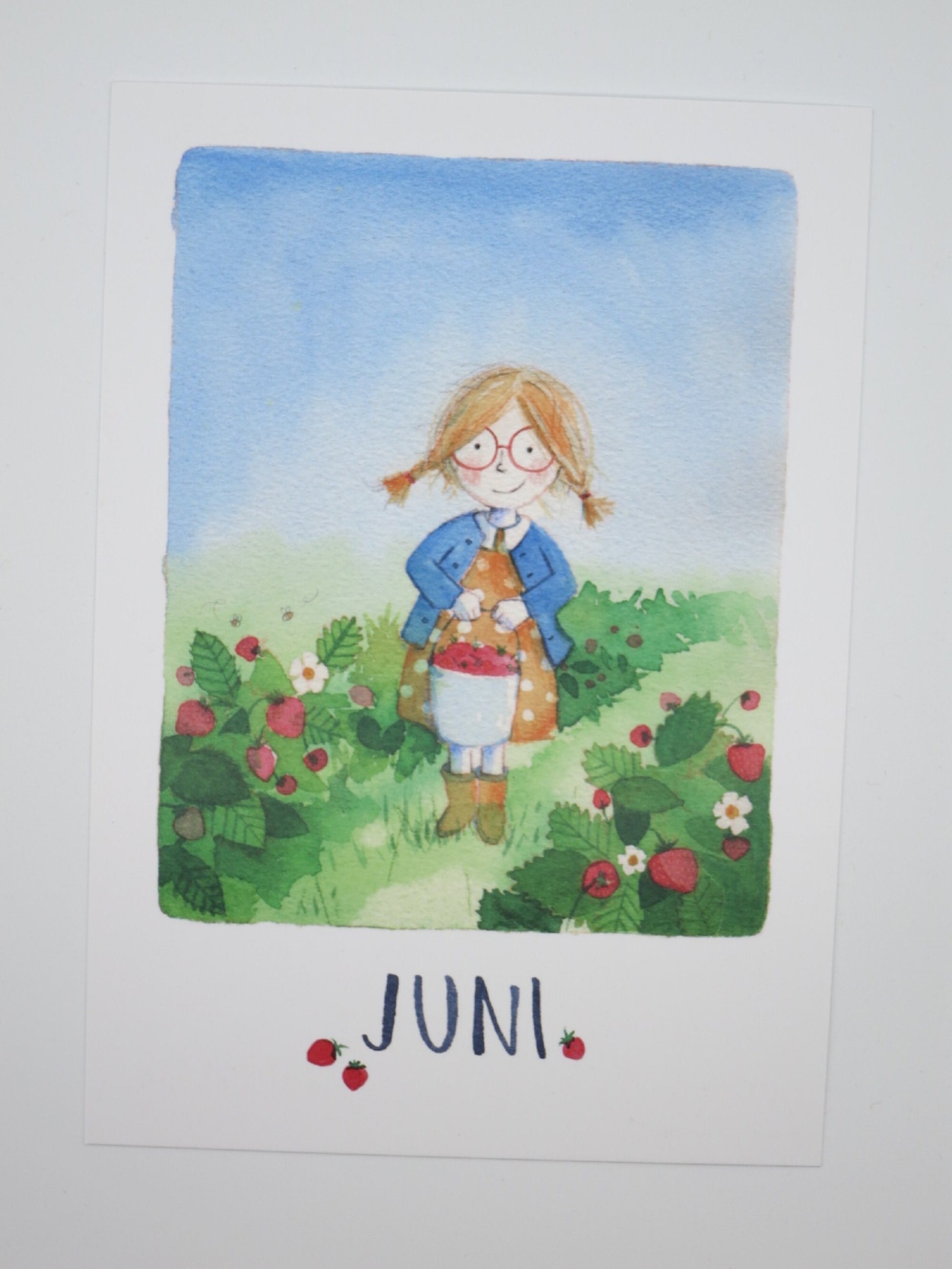 Waldorf Postkarte Juni: Mädchen mit Brille sammelt Walderdbeeren in der Schürze, Aquarell von Stefanie Messing