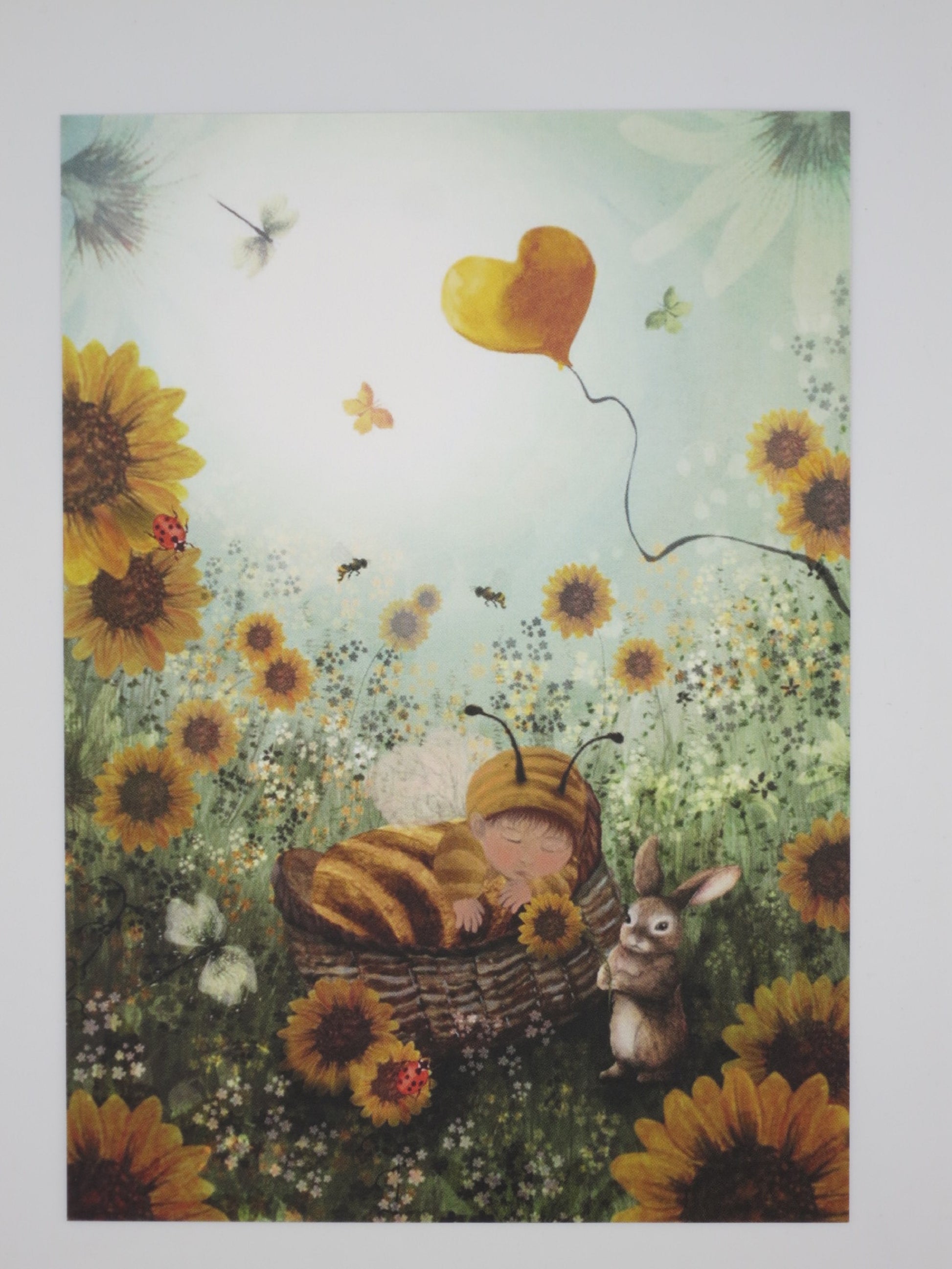 Postkarte Kleine Honigbiene: schlafendes Baby im Bienenkostüm zwischen Sonnenblumen, Illustration von Bijdehansje