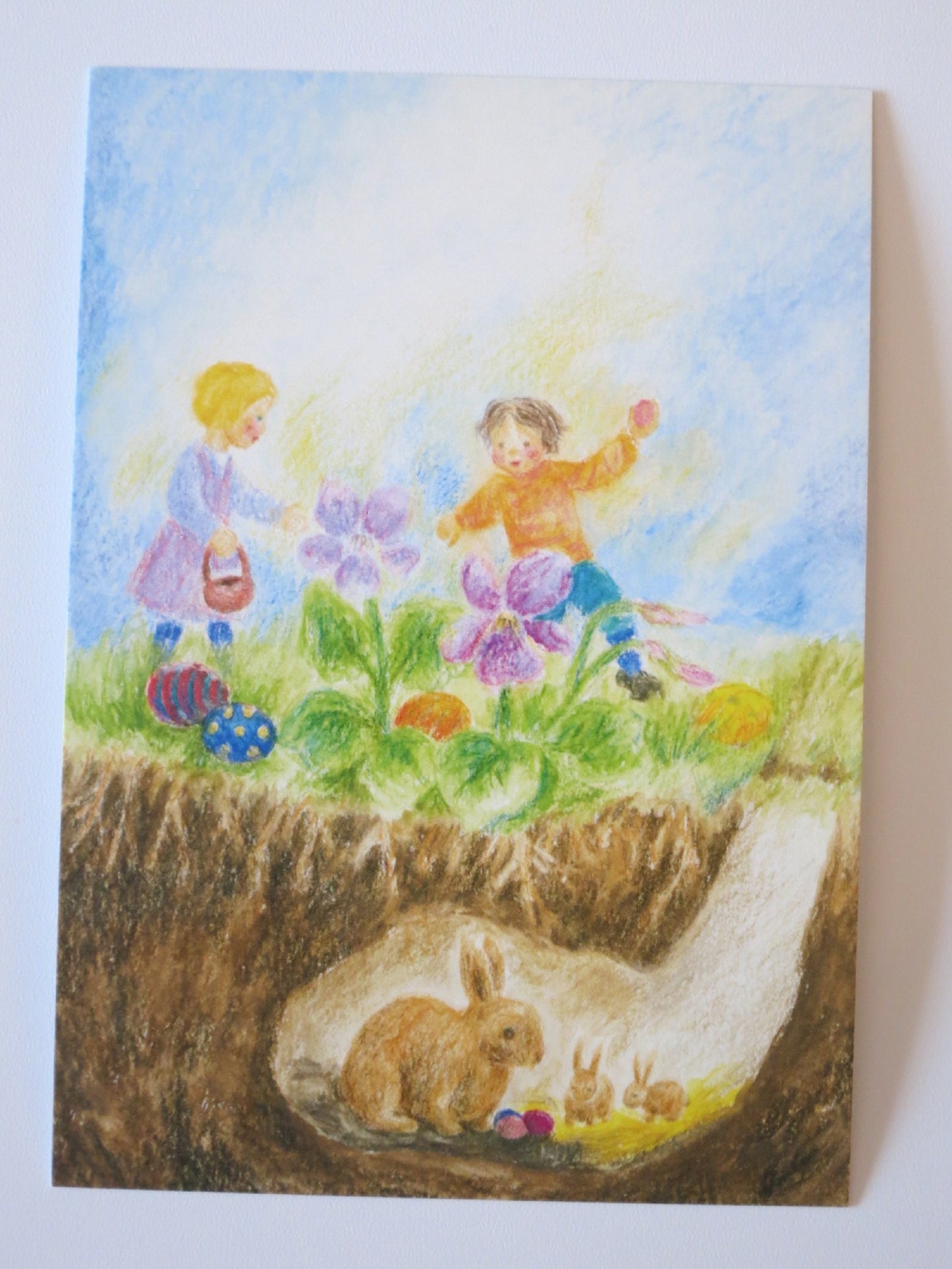 Waldorf Postkarte Ostern von Ilona Bock: Kinder oben und Hasenfamilie im Kaninchenbau unten