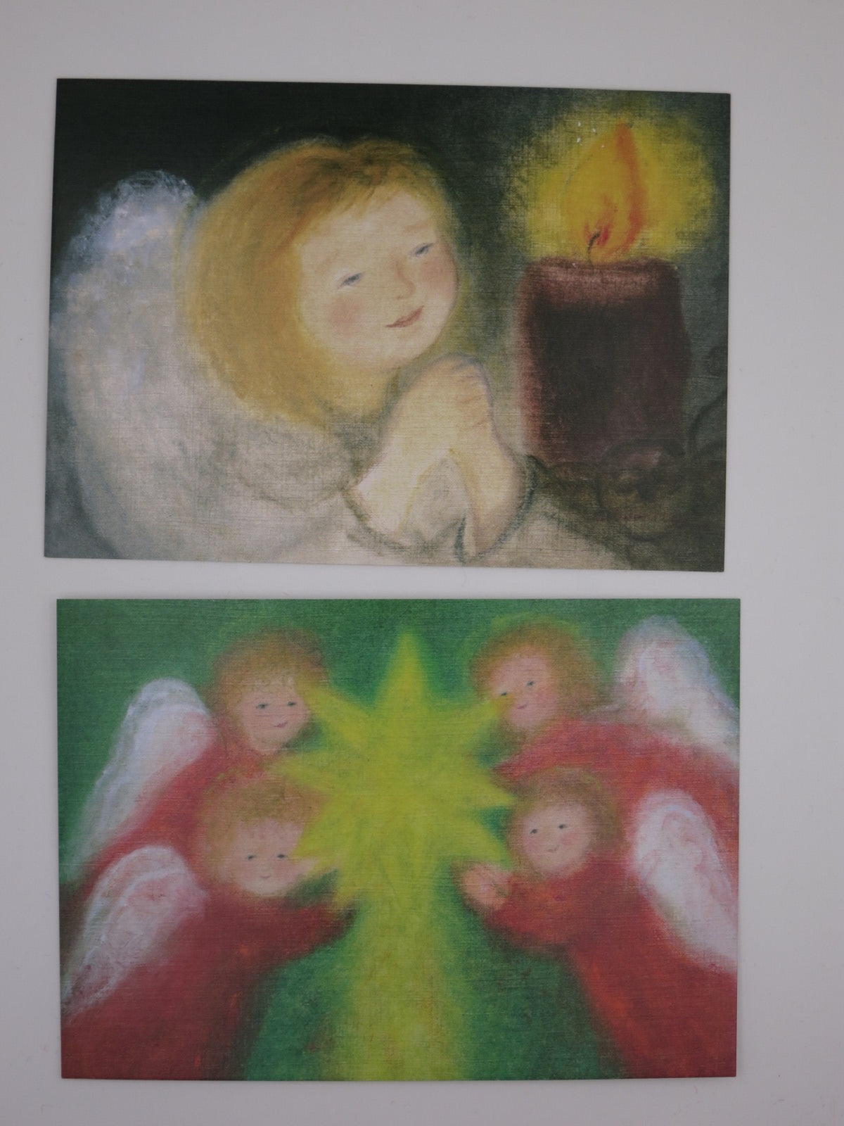 Zwei Karten aus dem Postkartenset Winter: Engel mit Kerze und rote Engel um einen Stern