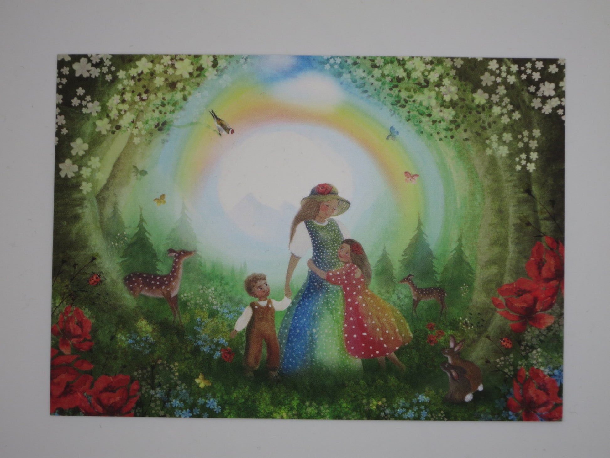 Postkarte Regenbogenwiese von Bijdehansje mit Mutter und Kindern unter einem Regenbogen im Wald mit Rehen und Kaninchen