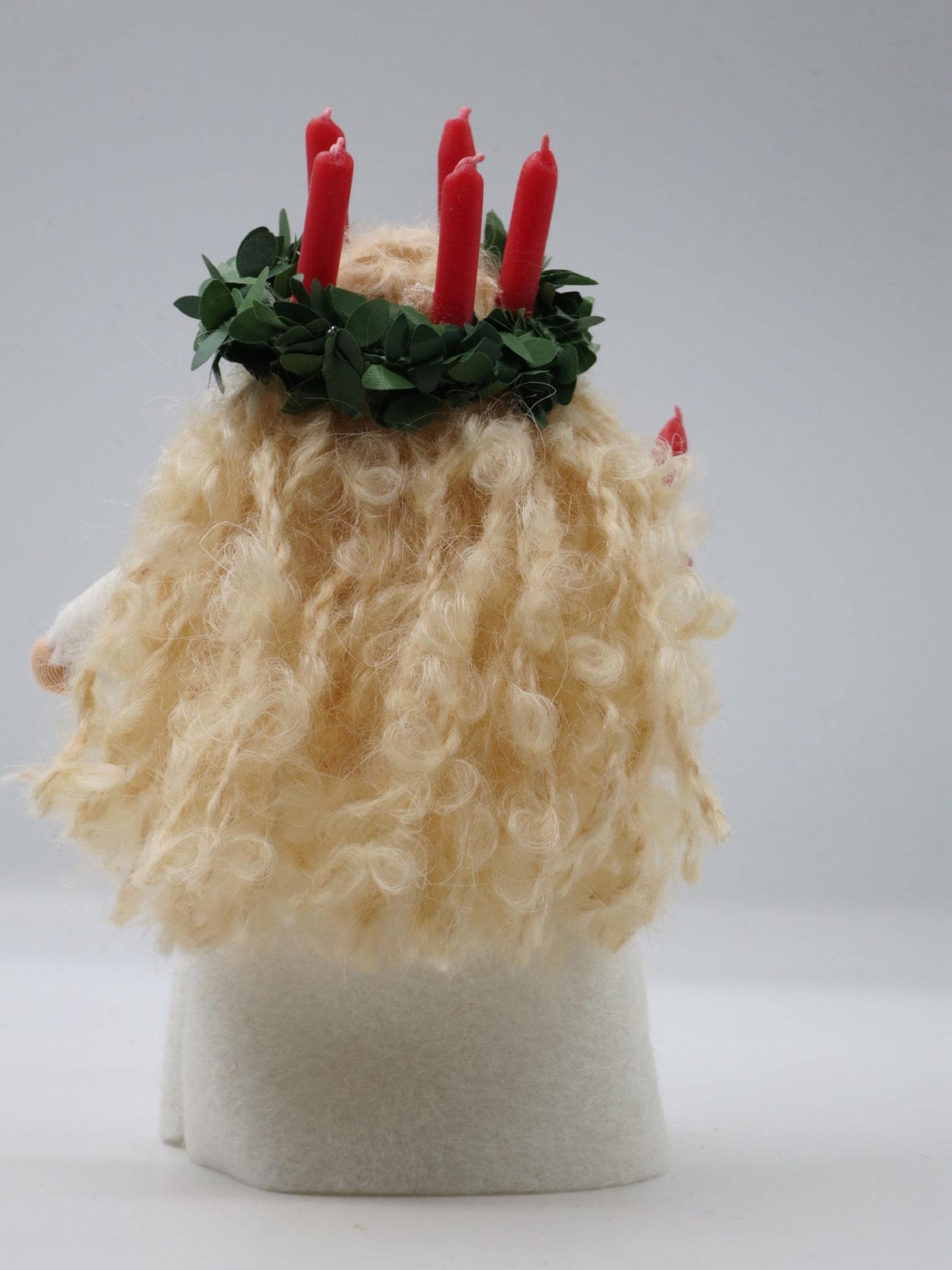 Rückansicht des Santa-Lucia-Blumenkinds mit Kerzenkranz und blondem Lockenhaar über dem weißen Wollfilzkleid.