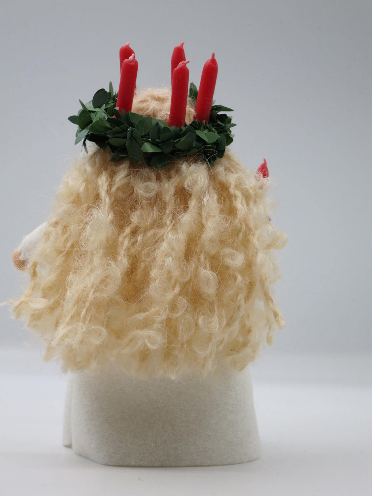 Rückansicht des Santa-Lucia-Blumenkinds mit Kerzenkranz und blondem Lockenhaar über dem weißen Wollfilzkleid.