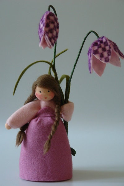 Rückansicht der Schachbrettblumen-Figur mit langem Zopf und Blütenzweig.
