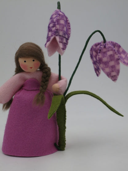 Seitenansicht der Schachbrettblumen-Figur mit magentafarbenem Kleid und Blütenzweig.