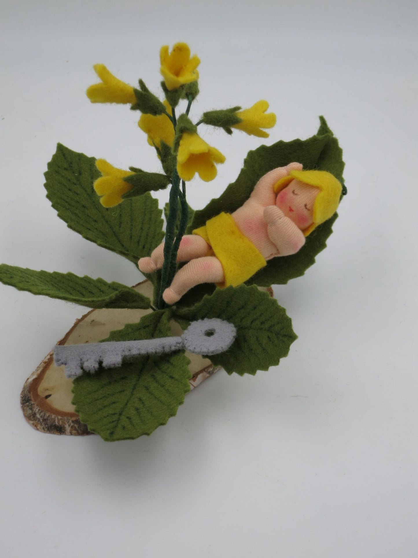 Schlüsselblumen Baby Blumenkind aus Wollfilz für den Waldorf Jahreszeitentisch, schlafend im Blatt neben gelber Schlüsselblume und kleinem Filzschlüssel