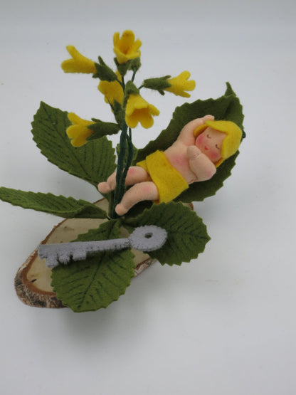 Schlüsselblumen Baby Blumenkind aus Wollfilz für den Waldorf Jahreszeitentisch, schlafend im Blatt neben gelber Schlüsselblume und kleinem Filzschlüssel