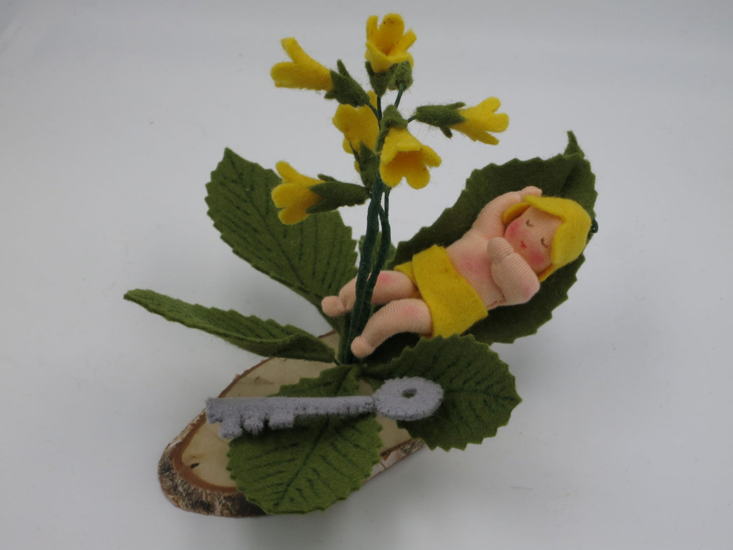 Schlüsselblumen Baby mit gelber Blütenrispe und Filzschlüssel auf Holzscheibe, Seitenansicht