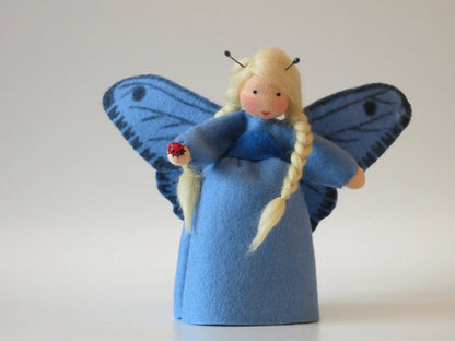 Blaues Schmetterling-Blumenkind mit gepunkteten Flügeln und Marienkäfer-Holzfigur in der Hand