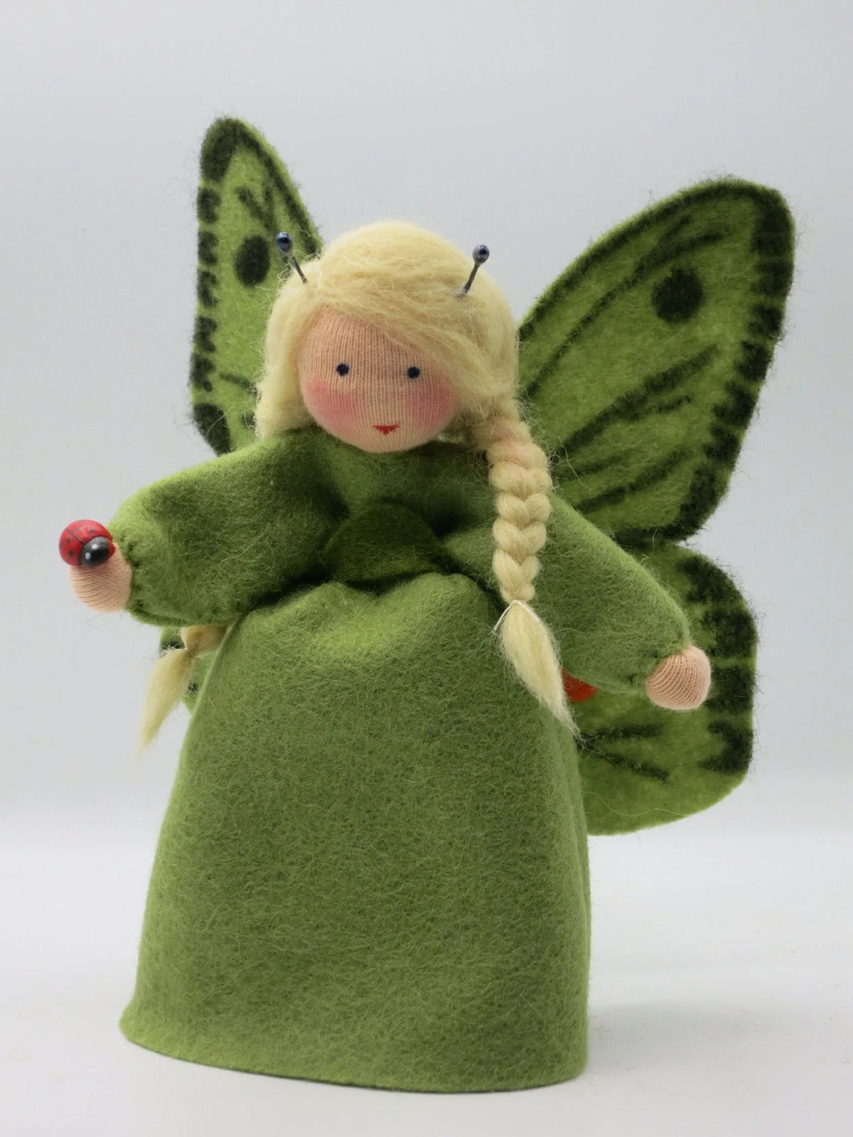 Grünes Schmetterling-Blumenkind mit gepunkteten Flügeln und kleiner Marienkäfer-Holzfigur in der Hand