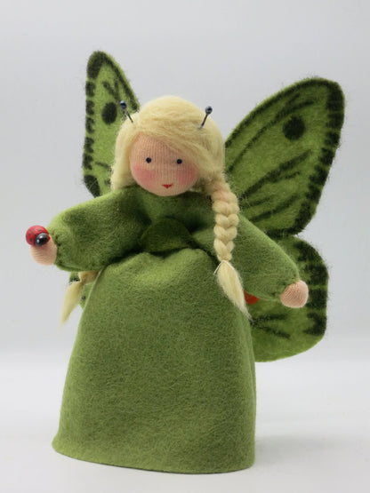 Grünes Schmetterling-Blumenkind mit gepunkteten Flügeln und kleiner Marienkäfer-Holzfigur in der Hand