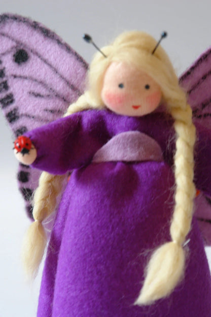 Lila Schmetterling-Blumenkind mit gepunkteten Flügeln, blondem Zopf und Marienkäfer-Figur