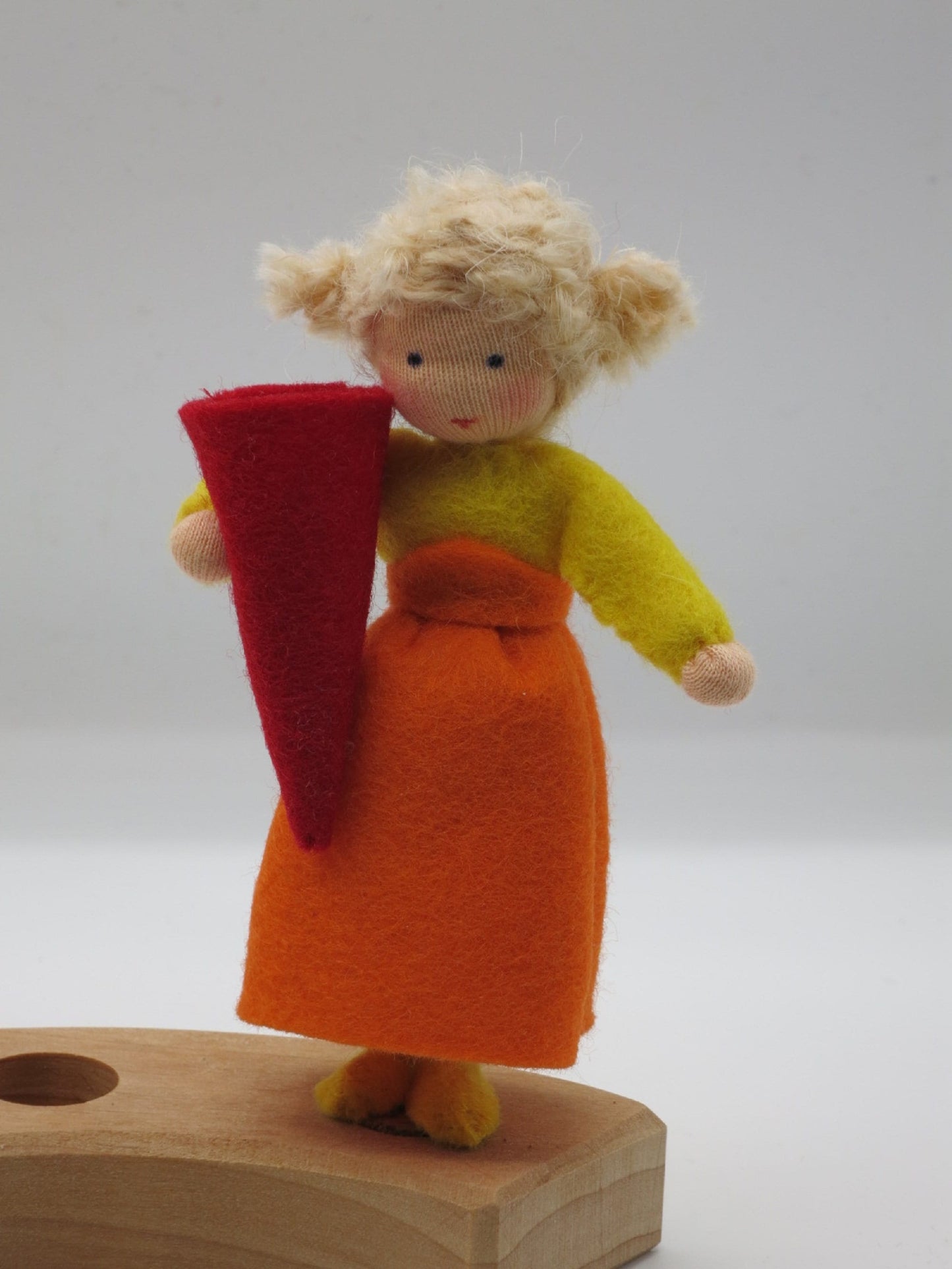Schulkind aus Wollfilz mit gelbem Oberteil, orangefarbenem Rock und roter Zuckertüte auf einem Holz-Geburtstagsring.