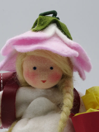 Gesichtsdetail des Schulmädchens mit rosa Rosenblütenhut und rotem Lederranzen aus Wollfilz.