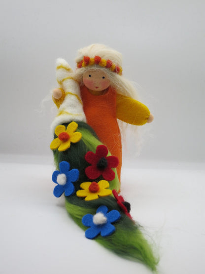 Handgefertigte Sommerfigur in Orange und Gelb mit grünem Filzteppich und bunten roten, gelben und blauen Blumen