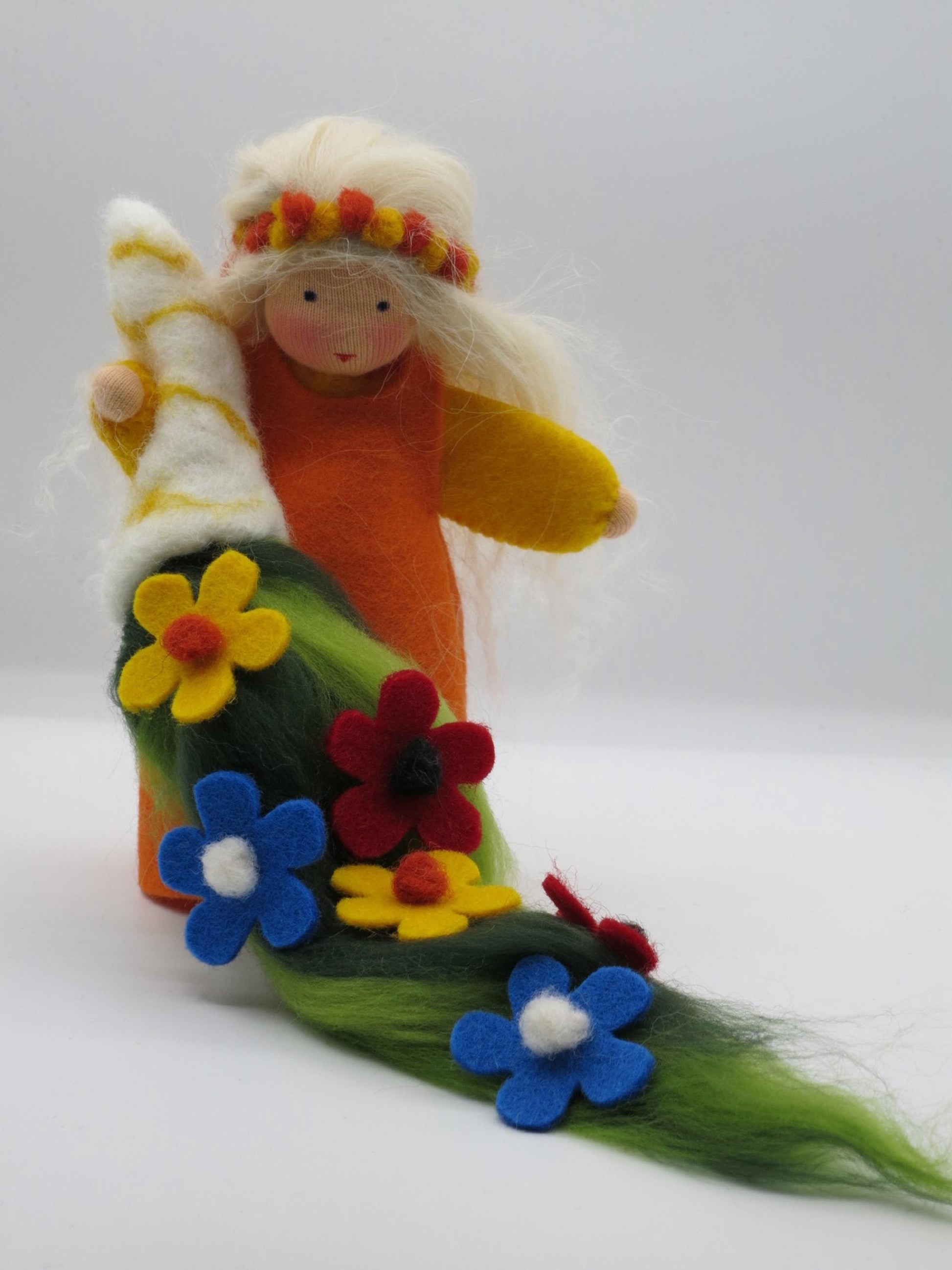 Sommer-Blumenkind mit blondem Wollhaar und grünem Blumenteppich aus blauen, roten und gelben Filzblüten