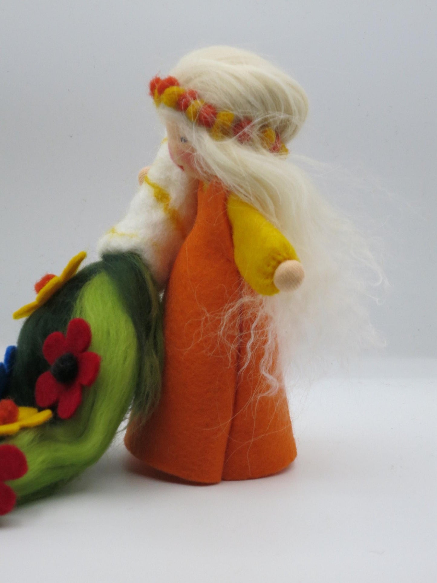 Sommerfigur im Profil mit orangefarbenem Filzkleid, gelbem Arm, langem blondem Wollhaar und Blumenteppich