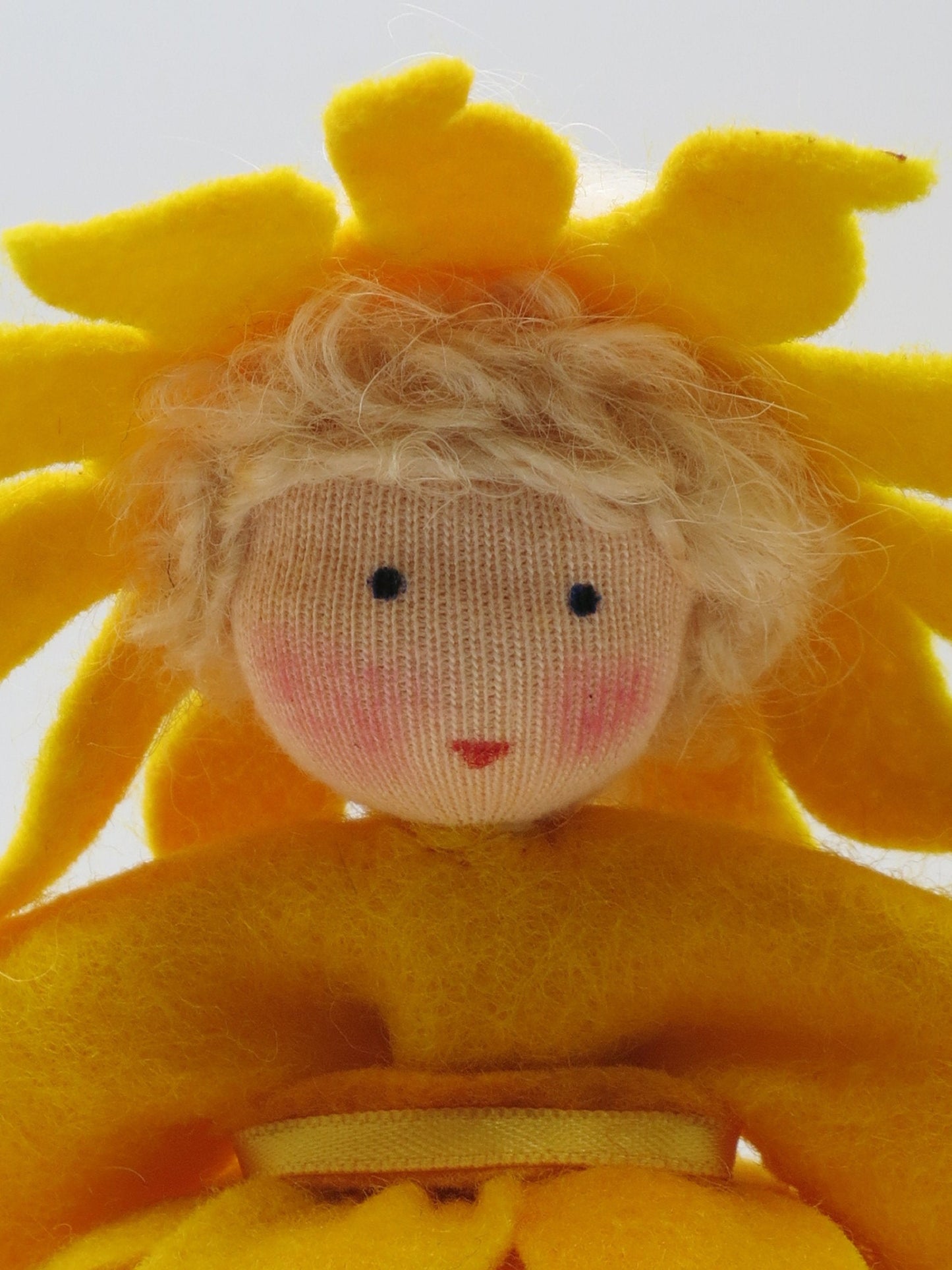Gesichtsdetail des Sonnen-Mädchens mit lockigem Haar und gelbem Strahlenkranz aus Wollfilz.