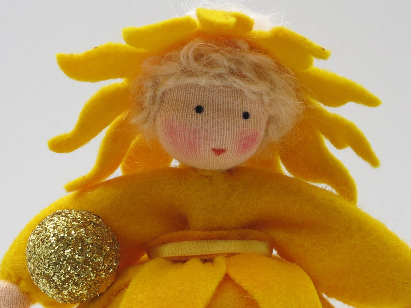 Nahaufnahme von Gesicht und goldener Sonnenkugel des Sonnen-Mädchen-Blumenkinds aus Wollfilz.