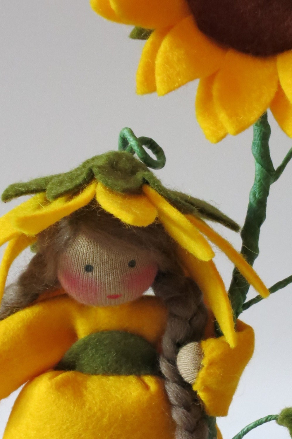 Zweite Nahaufnahme des Sonnenblumen-Gesichts mit braunem Zopf und gelbem Blütenhütchen.