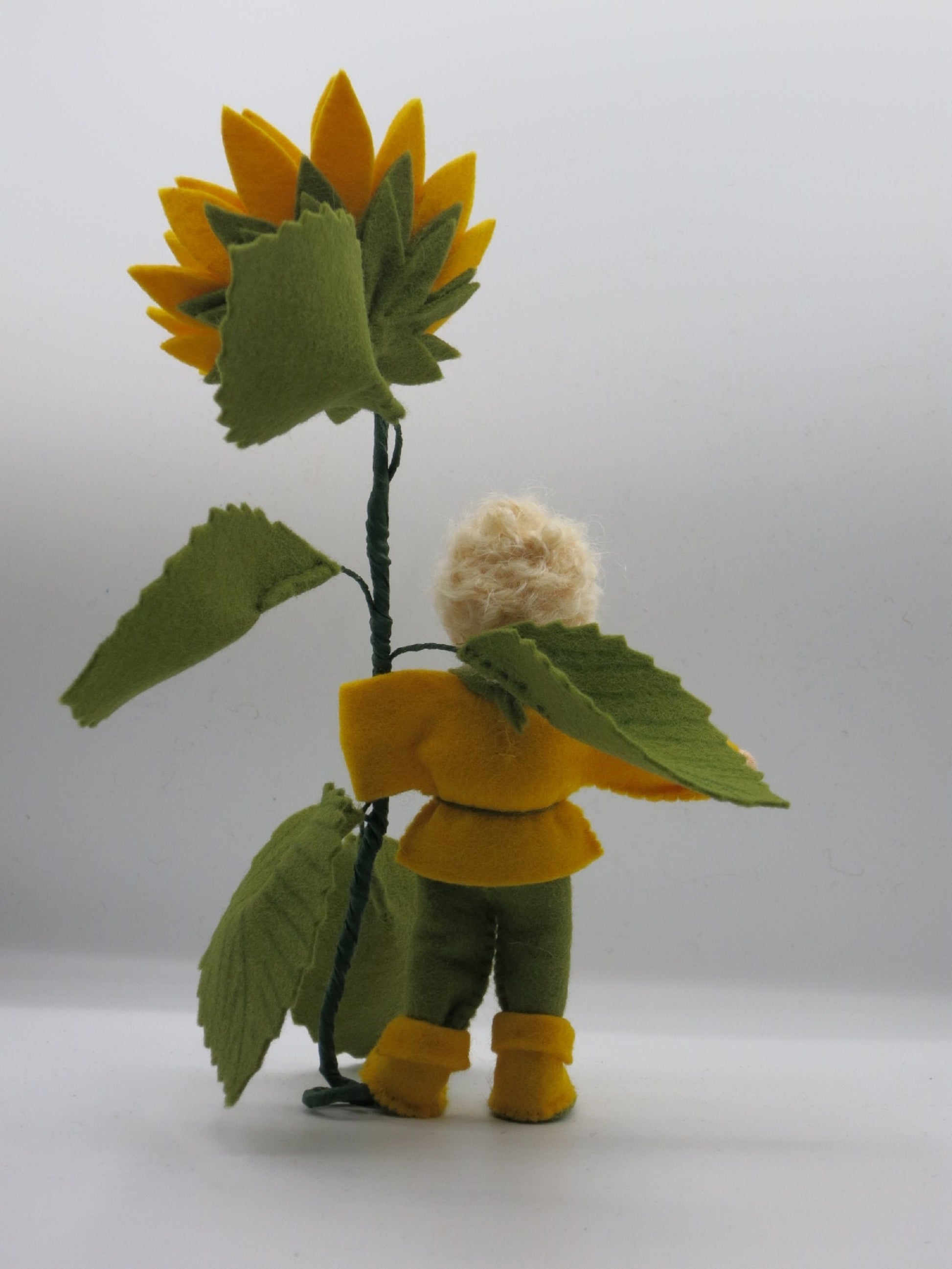 Rückansicht des Sonnenblumen-Jungen mit blondem Lockenhaar und gelben Filzstiefeln.