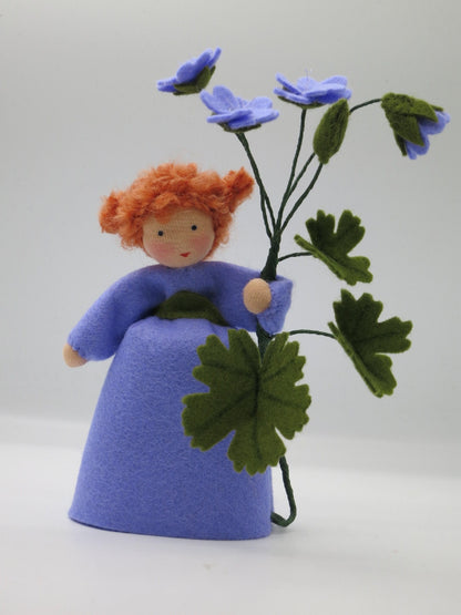 Storchschnabel-Blumenkind aus Wollfilz für den Waldorf Jahreszeitentisch mit drei violetten Blüten und gelappten Blättern.