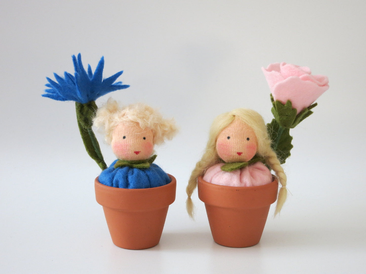 Rosen- und Kornblumen-Blumenkind mit rosa und blauer Filzblüte in zwei kleinen Terrakottatöpfen.