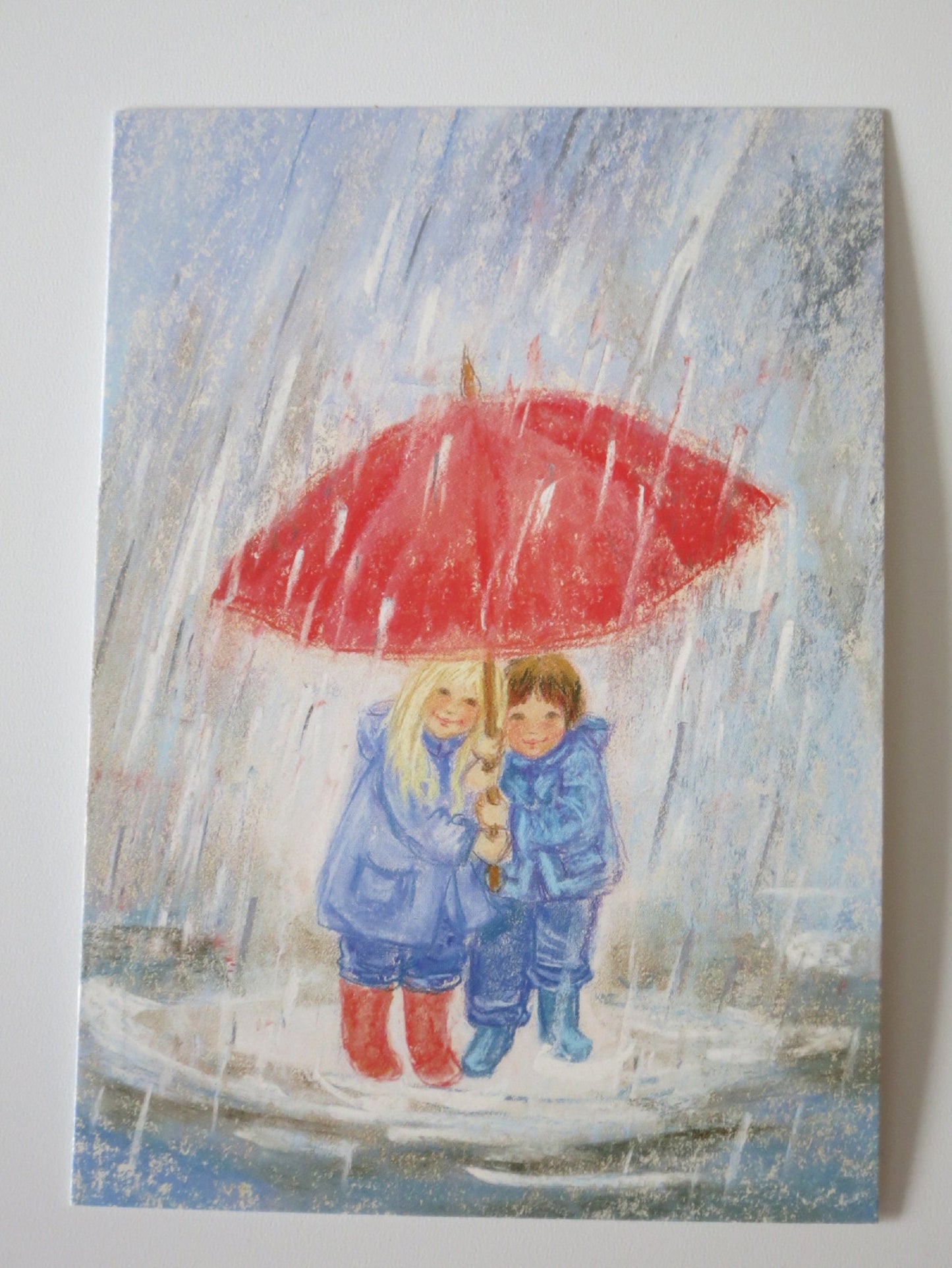 Zwei Kinder unter rotem Regenschirm im strömenden Herbstregen – Waldorf Postkarte von Marjan van Zeyl