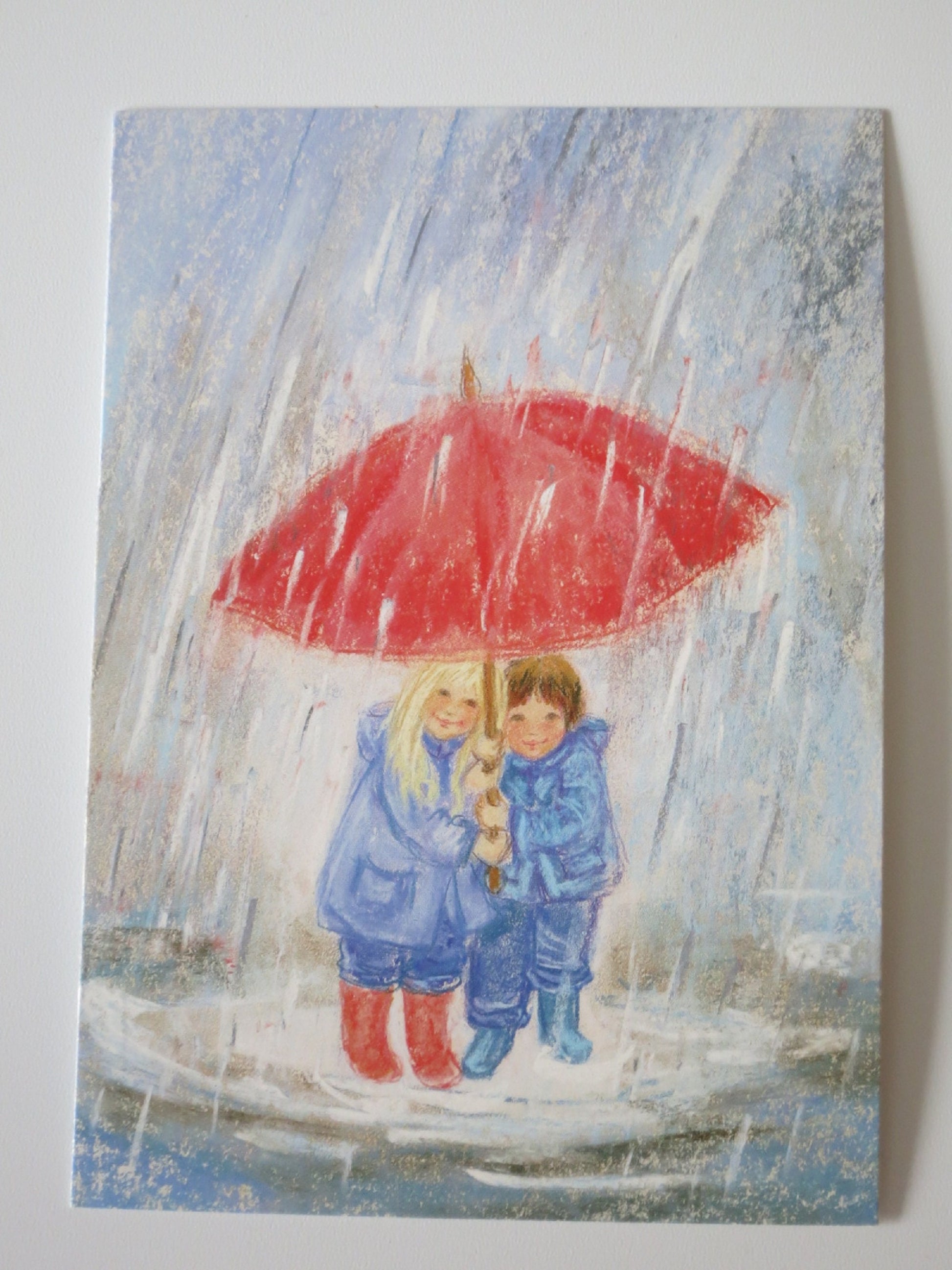 Zwei Kinder unter rotem Regenschirm im strömenden Herbstregen – Waldorf Postkarte von Marjan van Zeyl