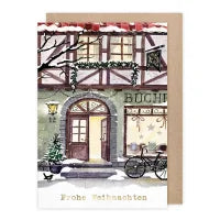 Weihnachtskarte mit Umschlag 'Frohe Weihnachten' von Anna Inspira: verschneites Fachwerkhaus mit Buchhandlung und Fahrrad.