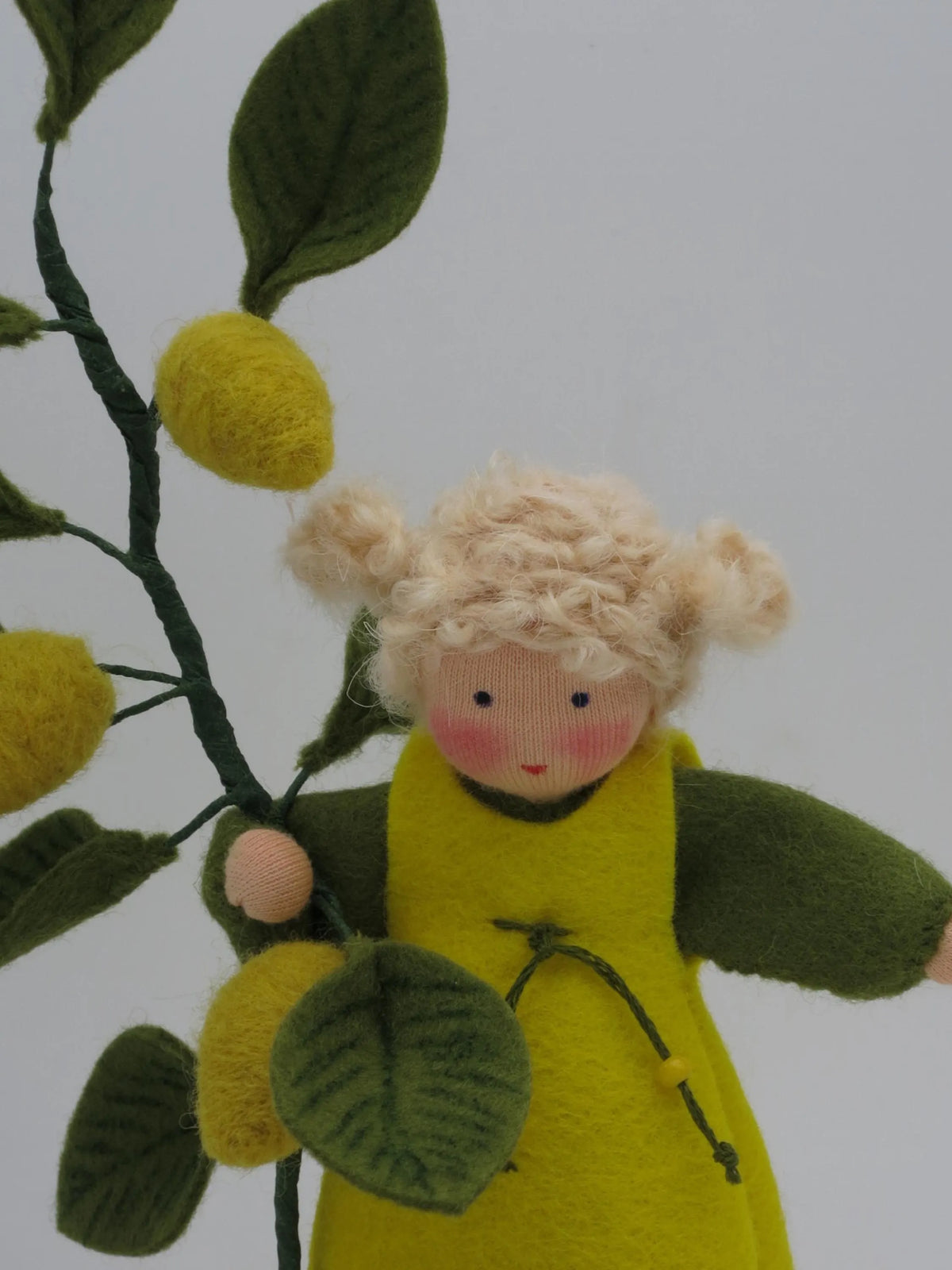 Detail des Zitronen-Blumenkinds: Hand am Zweig, gefilzte Zitrone und grüne Kordel mit Holzperle am Trägerkleid.
