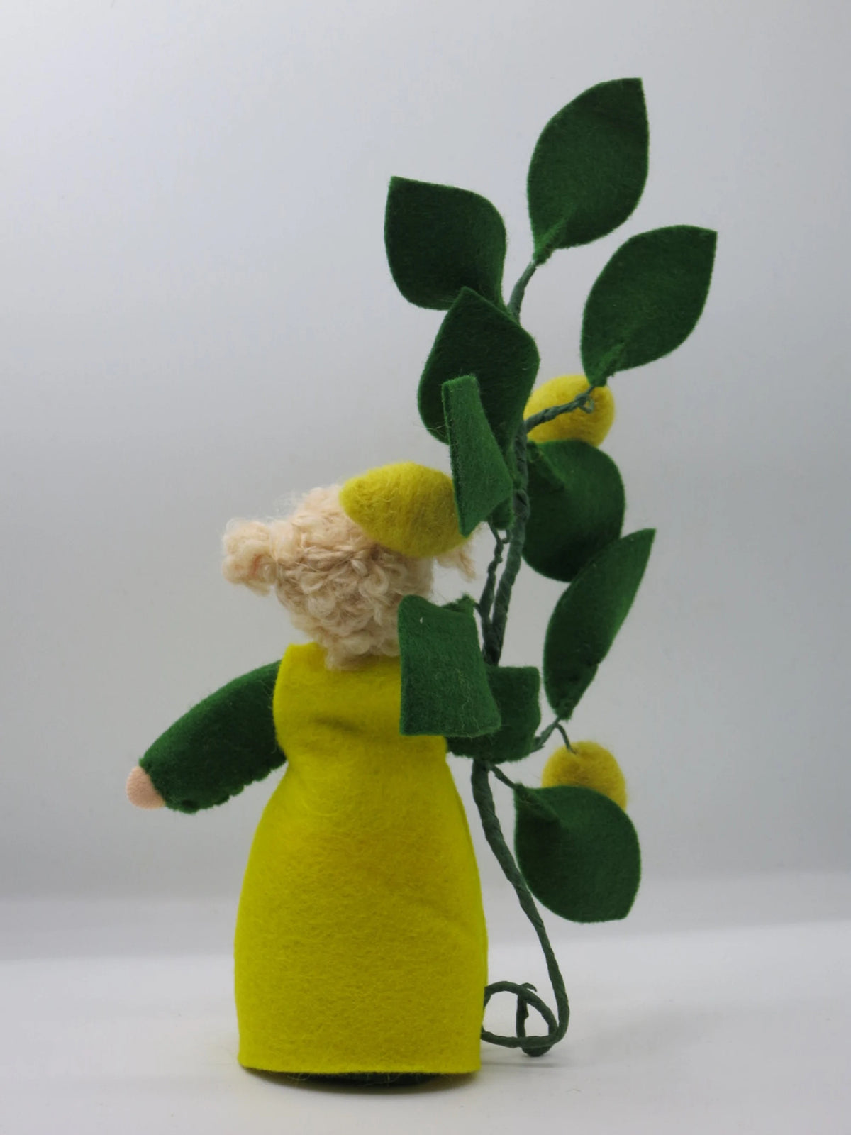 Rückansicht des Zitronen-Blumenkinds aus Wollfilz mit dunkelgrünen Filzblättern und gefilzten Zitronen am Drahtzweig.