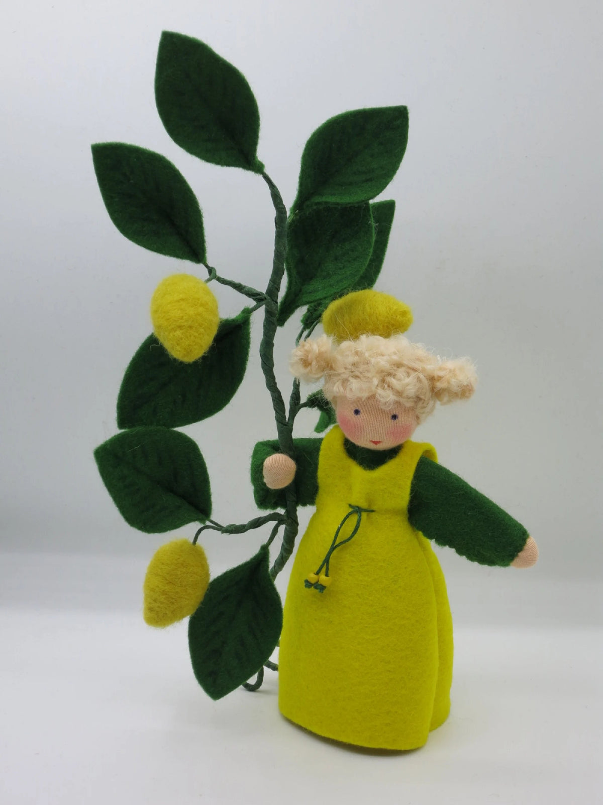 Zitronen-Blumenkind aus Wollfilz schräg von oben mit drei Zitronen und dunkelgrünen Blättern, Waldorf Jahreszeitentisch.