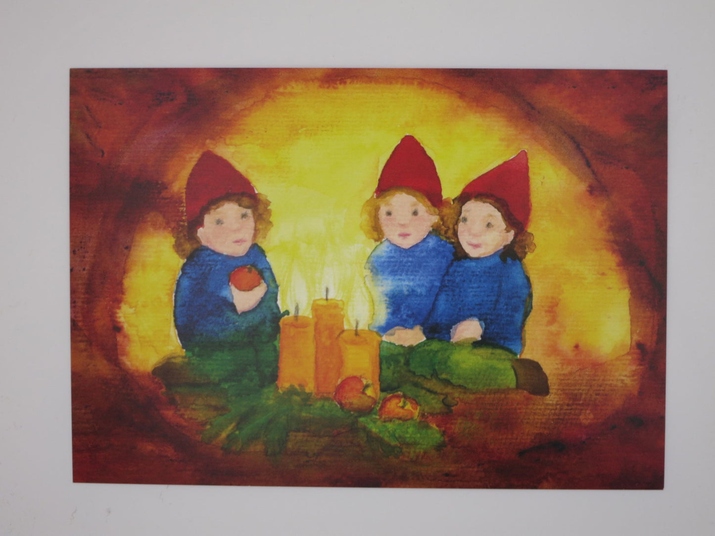 Postkarte Zwerge Aepfel und Kerzen von Anna Hunold, drei Zwerge sitzen um Kerzen und rote Aepfel
